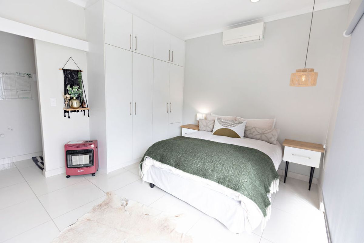 A well-maintained bedroom featuring neutral tiled flooring, ample built-in cupboard storage, and a wall-mounted split-system air conditioning unit.