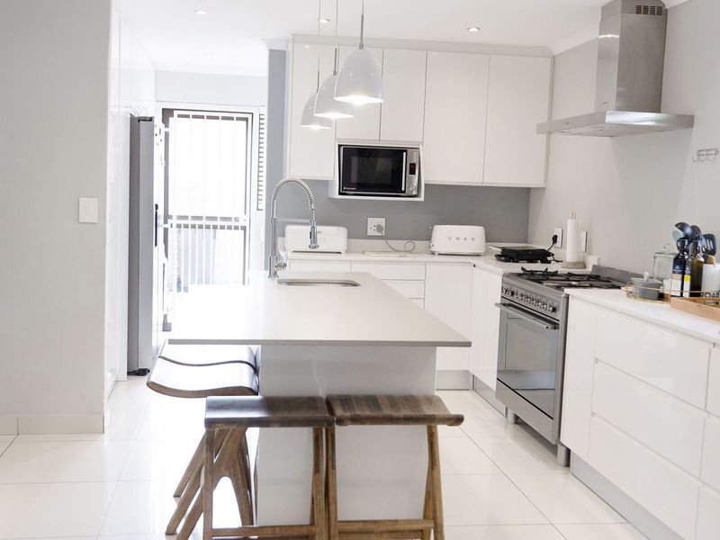 Modern kitchen featuring white cabinetry, a central island with breakfast bar, stainless steel appliances, and sleek tiled flooring.