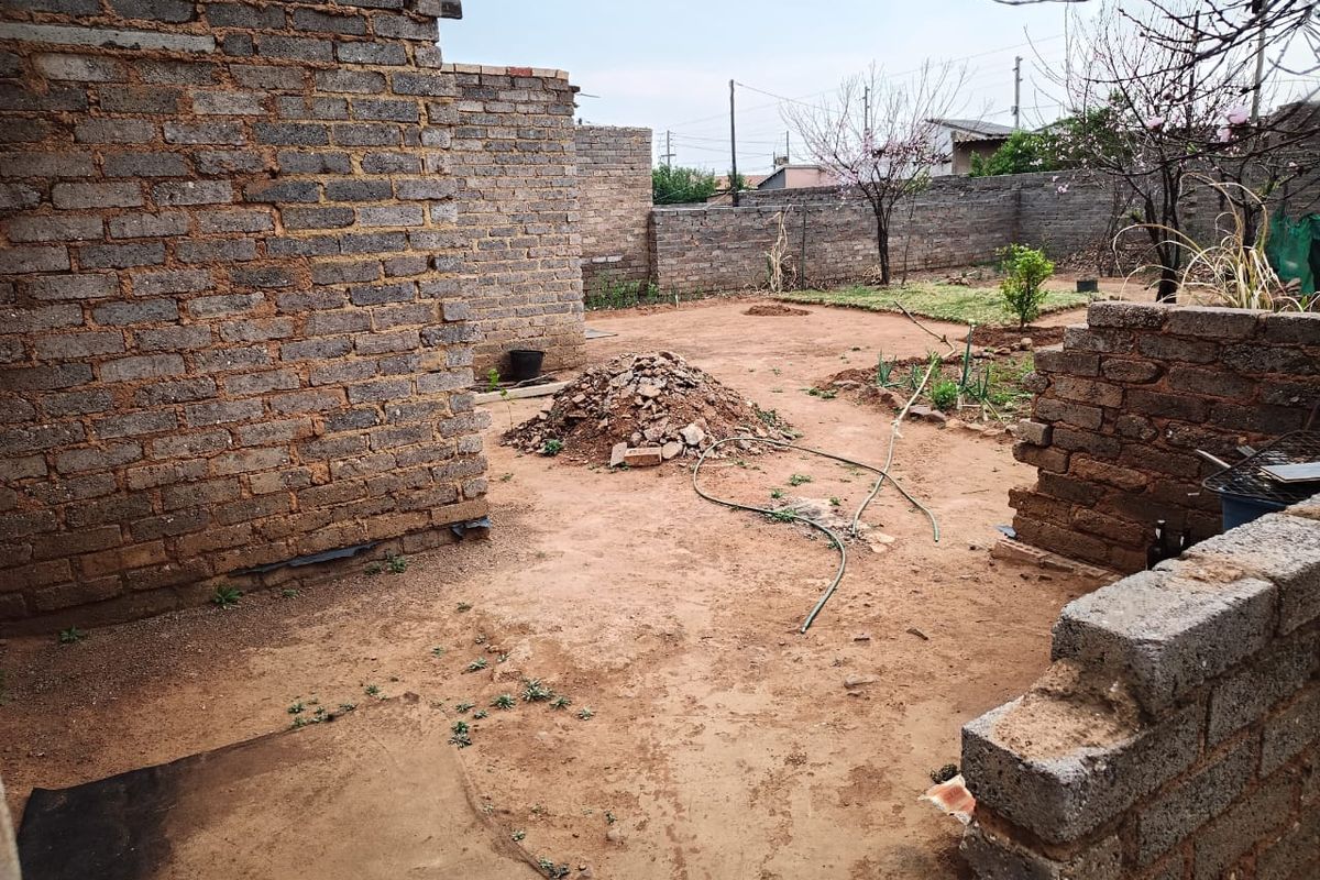A rear yard area featuring unfinished brick walls and an open dirt plot, requiring significant landscaping and construction completion.