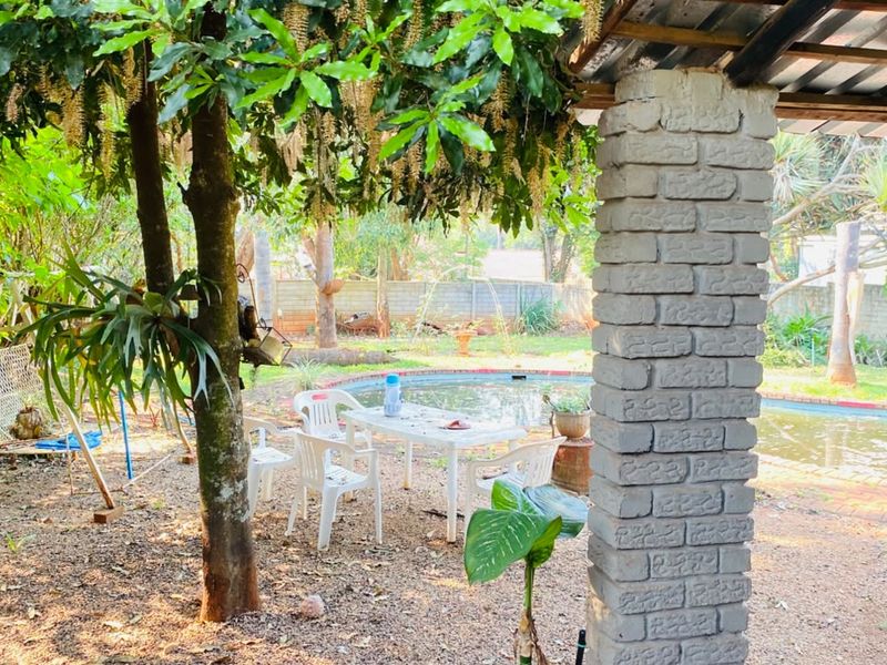 Outdoor pool area featuring a covered patio space with brick pillars, overlooking a swimming pool in a garden setting.