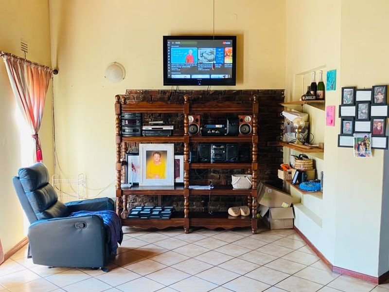 A living room featuring an exposed brick wall section, built-in shelving, and ceramic floor tiles, offering a functional space with potential for modern updates.
