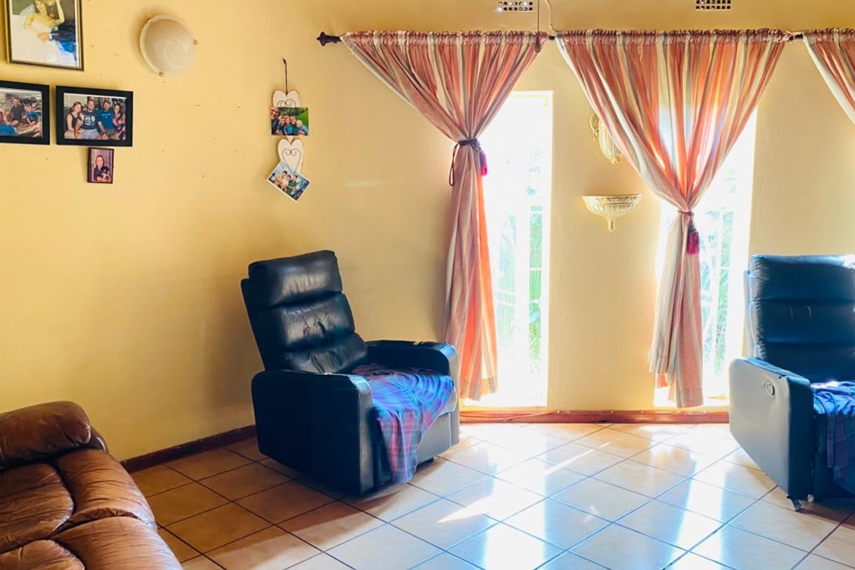 A living room featuring tiled flooring and natural light through large windows with curtain treatments.
