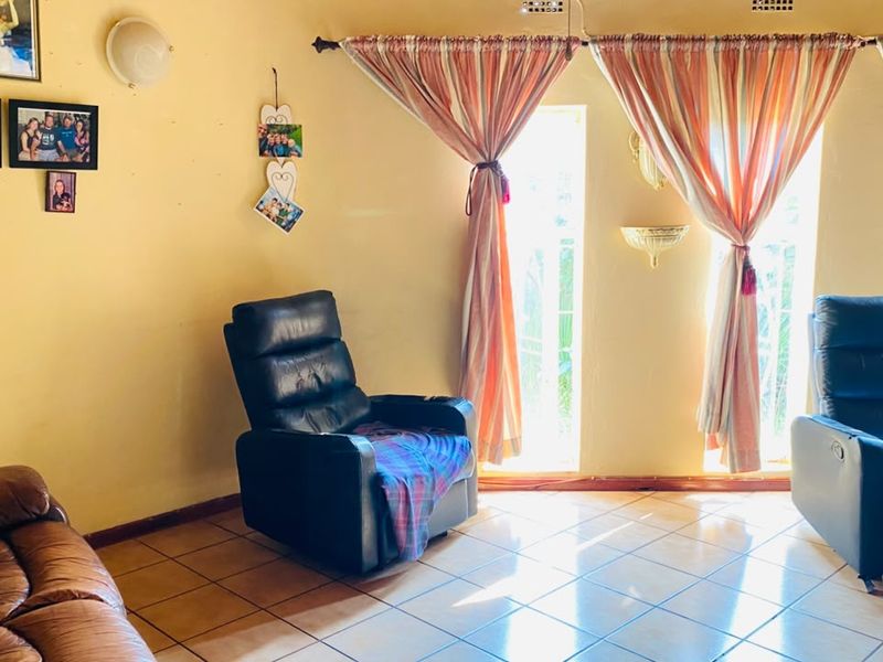 A living room featuring tiled flooring and natural light through large windows with curtain treatments.
