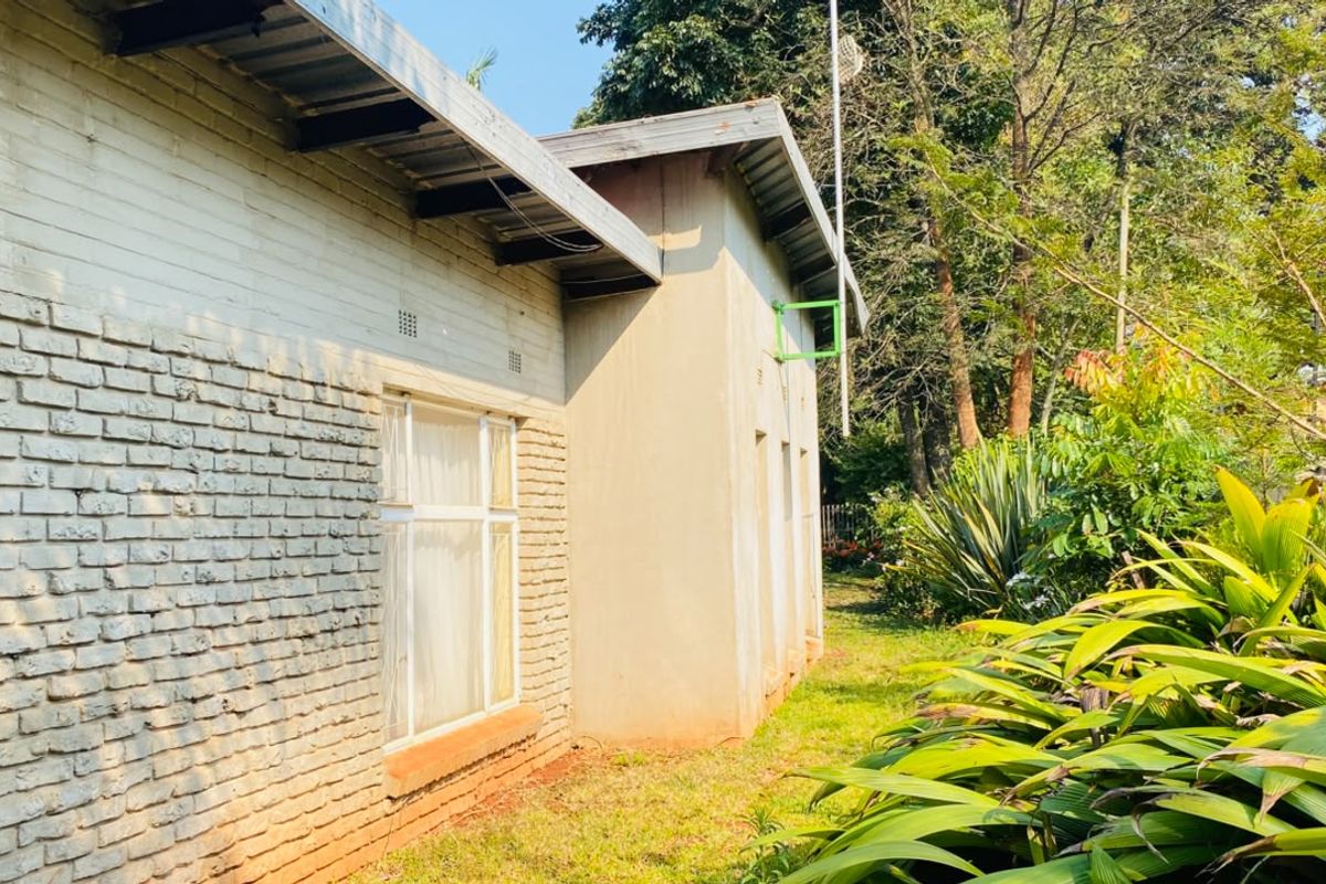 Rear view of the property featuring a brick facade, metal roofing, and established garden surroundings with security fencing.