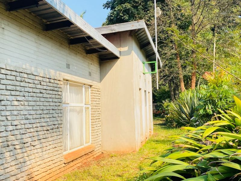 Rear view of the property featuring a brick facade, metal roofing, and established garden surroundings with security fencing.