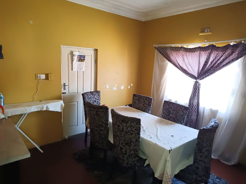 A dining room featuring yellow walls, coving, and a window with curtains. The space requires cosmetic updates to improve its overall condition.