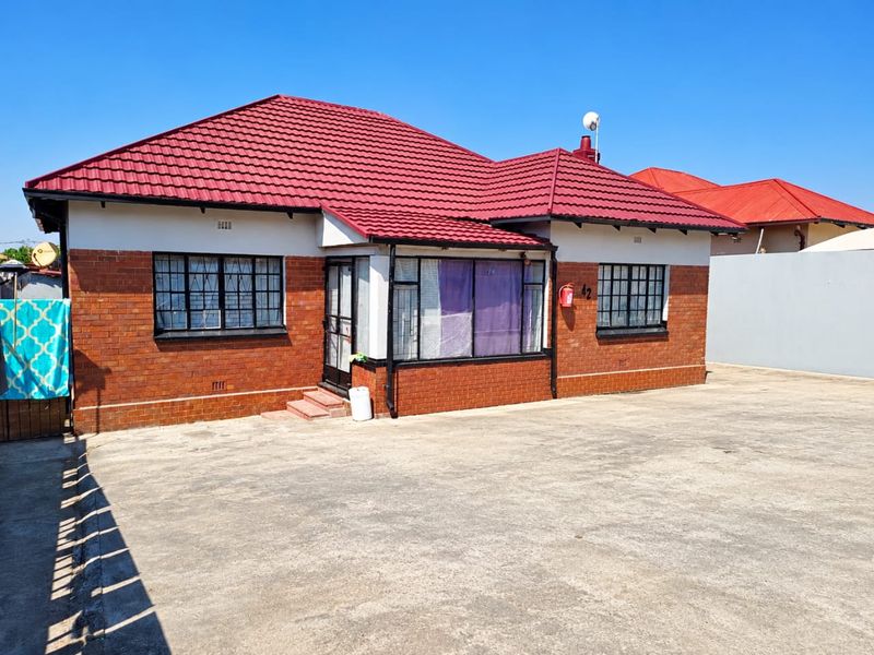 Front elevation of a single-story face brick house featuring a red tiled roof, security window bars, and a large concrete driveway.