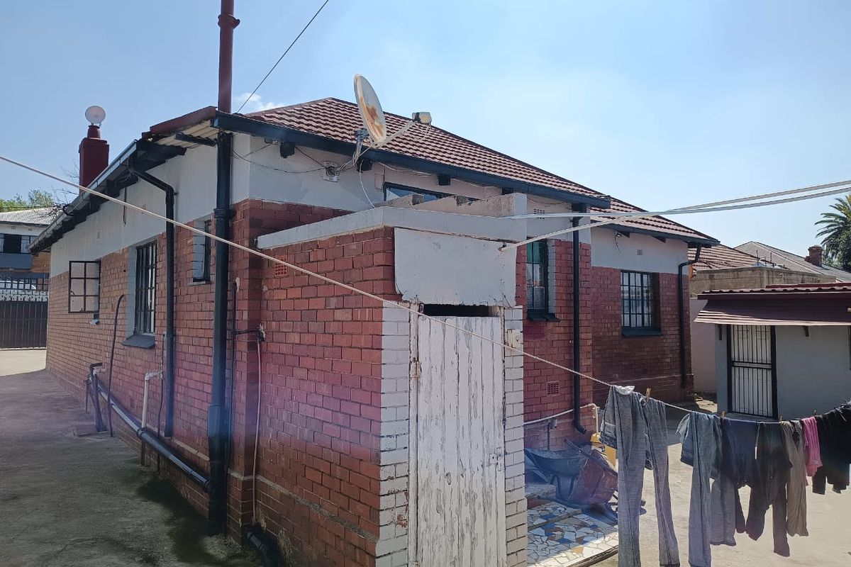 Rear view of a brick house featuring a tiled roof, chimney, and security bars on windows, with a small utility entrance area.
