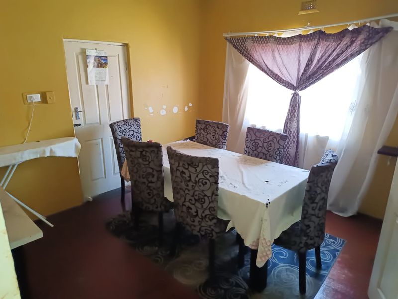 A dining room featuring yellow walls with visible surface wear and a window with curtain fixtures.