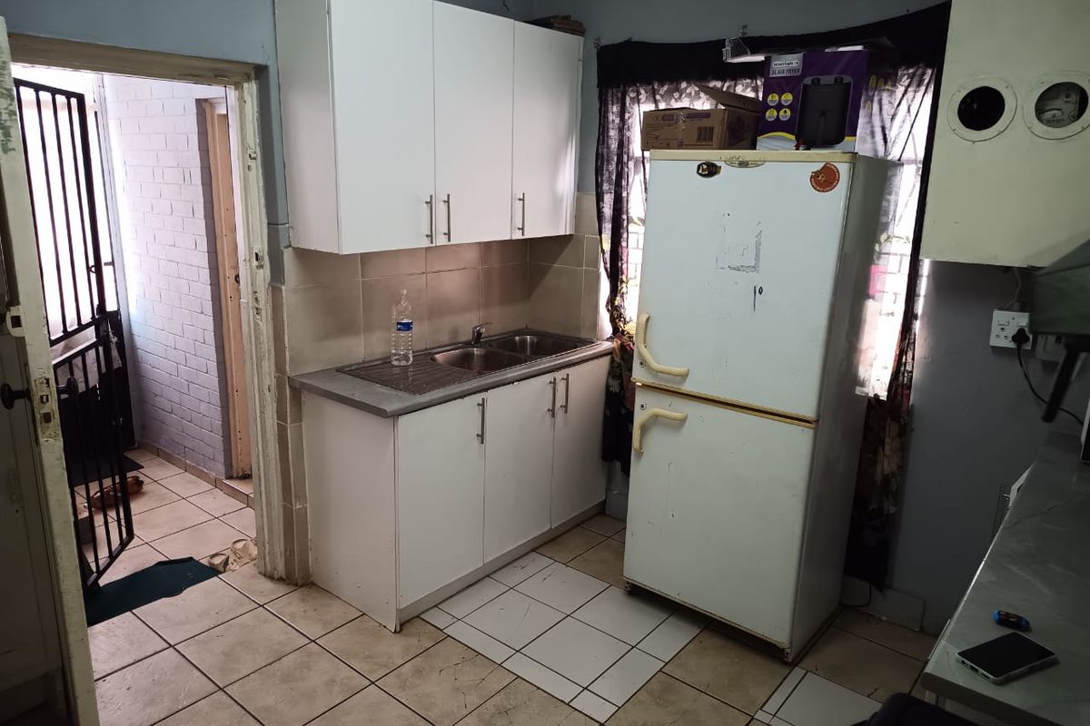 A compact kitchen area featuring white built-in cabinetry, a stainless steel sink, and tiled flooring, requiring cosmetic updates to improve its overall condition.