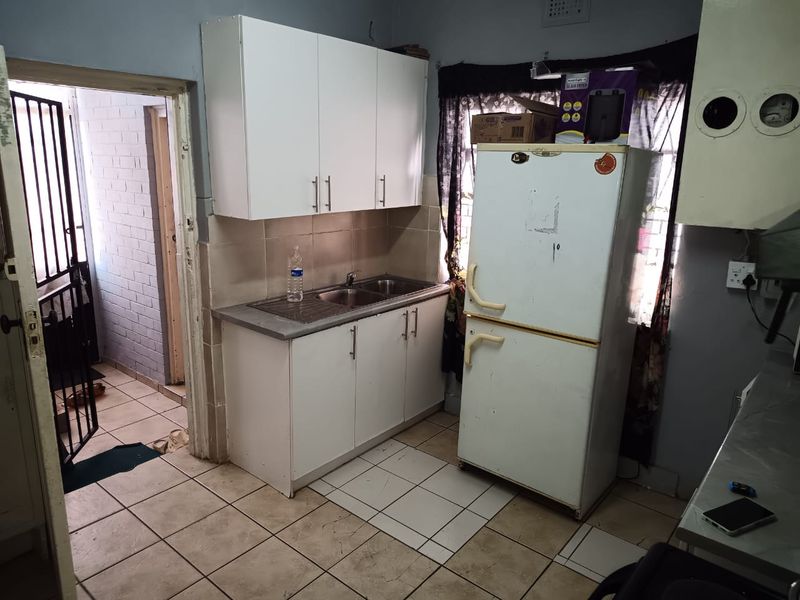 A compact kitchen area featuring white built-in cabinetry, a stainless steel sink, and tiled flooring, requiring cosmetic updates to improve its overall condition.
