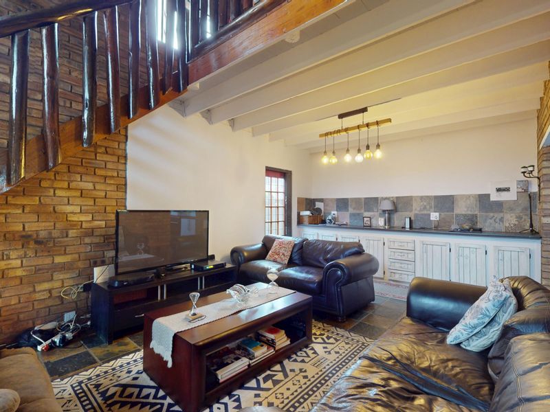 Open plan living area featuring exposed brick walls, timber staircase, exposed ceiling beams, and built-in cabinetry with stone tile backsplash.