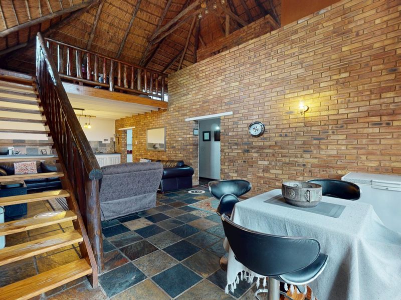 Open plan living area featuring high vaulted thatched ceilings, exposed brickwork, slate flooring, and a timber staircase leading to a mezzanine level.