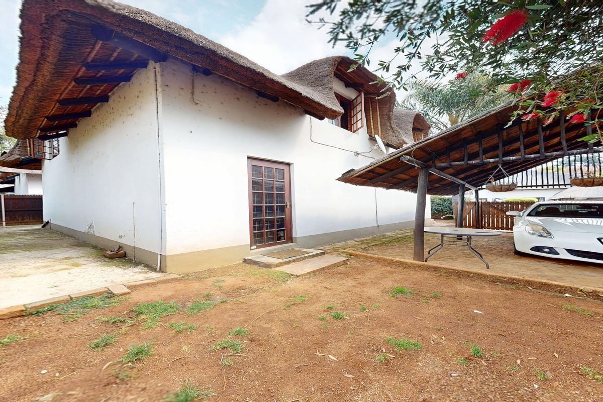Rear exterior view of a house featuring a traditional thatch roof, a timber carport structure, and a paved entrance area.