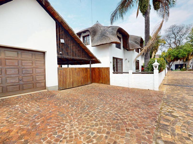 Front exterior view of a property featuring a distinctive thatched roof, brick paved driveway, and a secure wooden garage and gate entrance.
