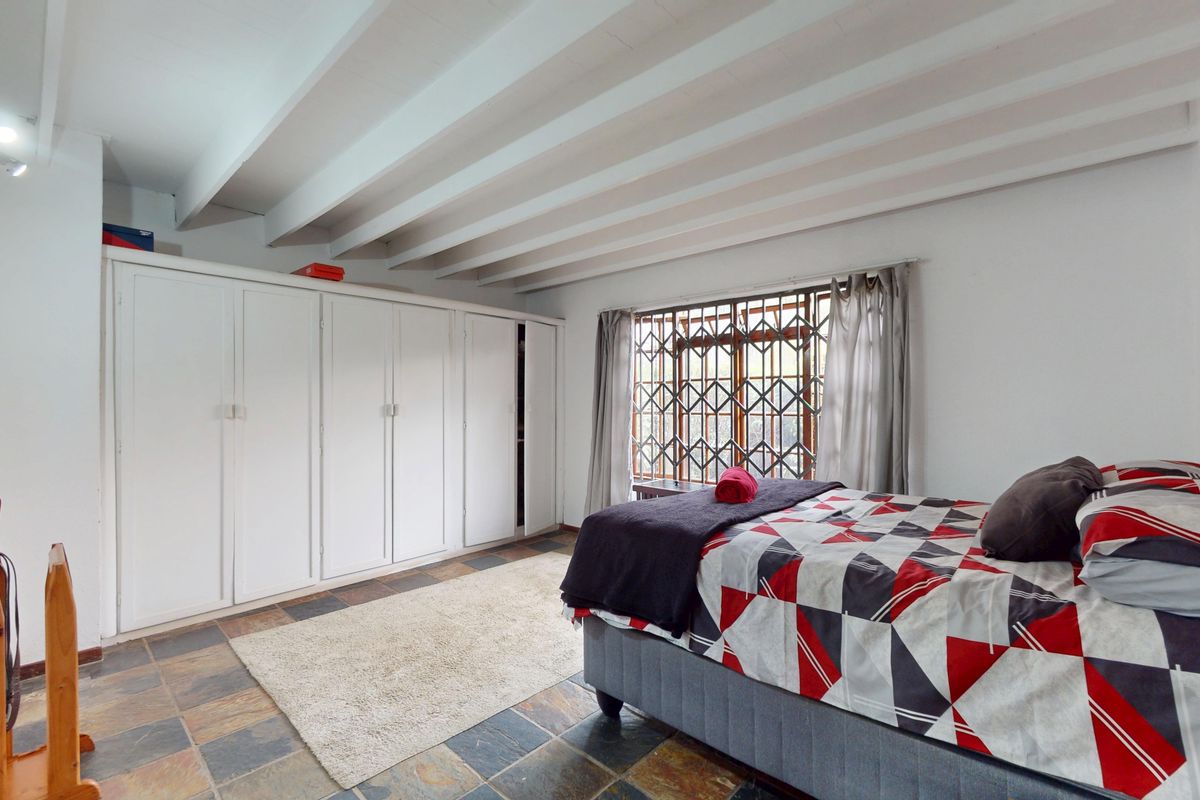 A bedroom featuring slate tile flooring, exposed beam ceilings, and extensive built-in cupboard storage, secured with a window gate.