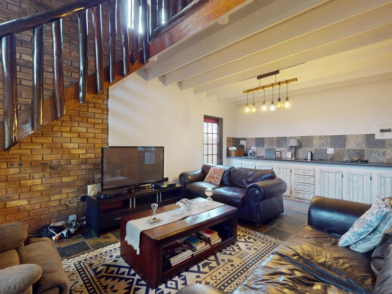 Open plan living area featuring exposed brick walls, a timber staircase, exposed beam ceilings, and built-in cabinetry with a tiled backsplash.
