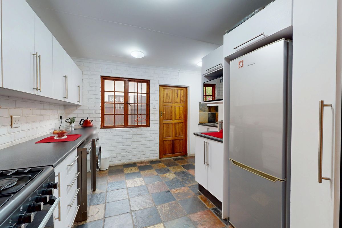 A functional kitchen featuring white cabinetry, dark laminate countertops, slate tile flooring, and an exposed brick wall with a timber door.