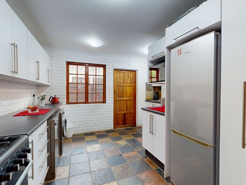 A functional kitchen featuring white cabinetry, dark laminate countertops, slate tile flooring, and an exposed brick wall with a timber door.