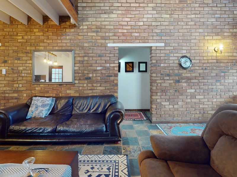 Spacious living room featuring a prominent exposed brick feature wall, rustic slate tile flooring, and exposed timber ceiling beams.