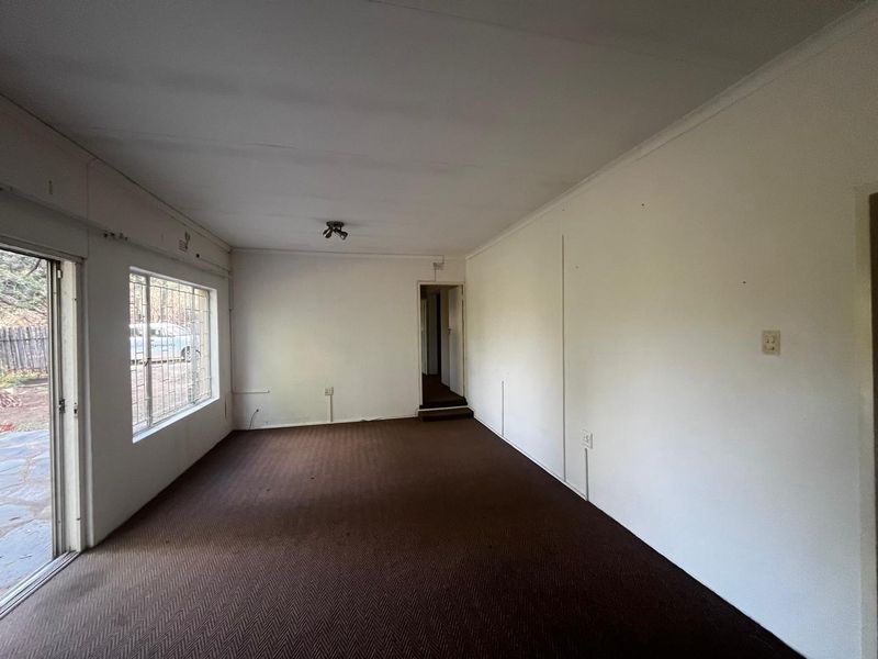 An empty living room featuring brown carpet flooring, a sliding glass door with security bars, and neutral walls.