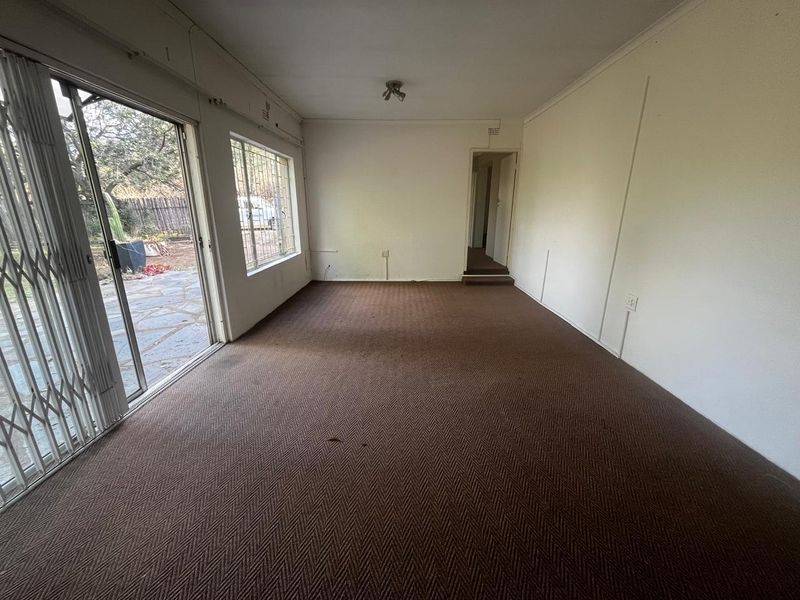 An empty living room featuring brown carpet flooring, a sliding glass door with a security gate, and large windows with security bars.