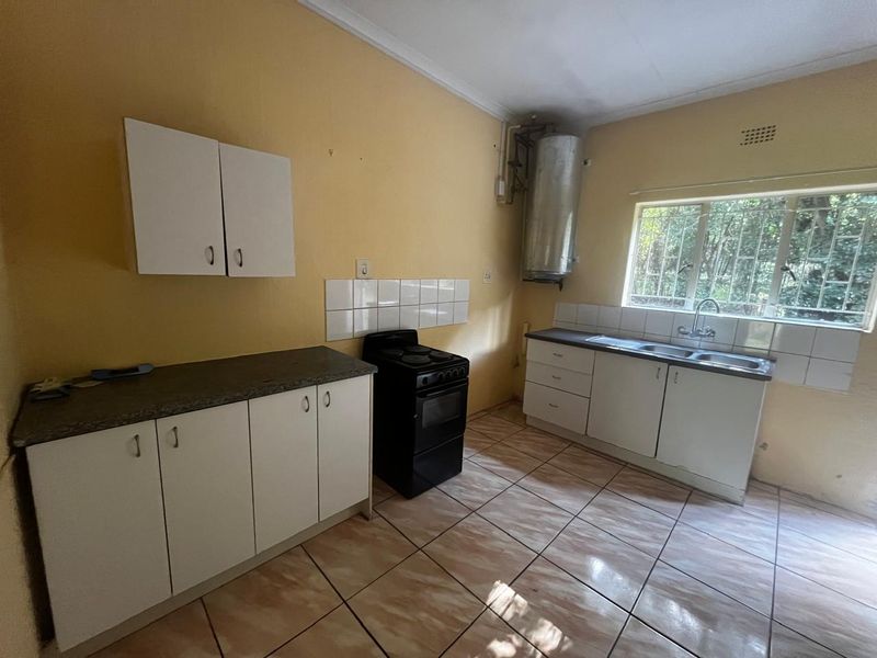 A functional kitchen featuring white cabinetry, tiled splashbacks, a double basin sink, and a freestanding stove, with tiled flooring throughout.