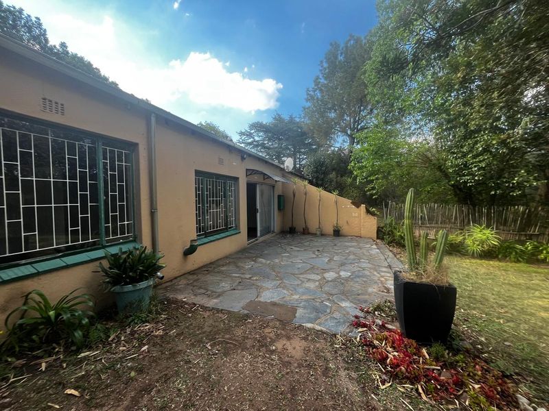 Rear exterior view of the cottage featuring a stone-paved patio area, sliding glass doors, and security bars on the windows.