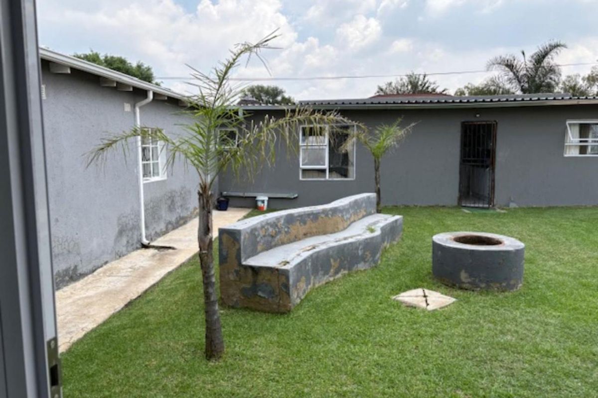 Rear garden area featuring a built-in concrete bench and fire pit, with lawn space and exterior access to the main dwelling.