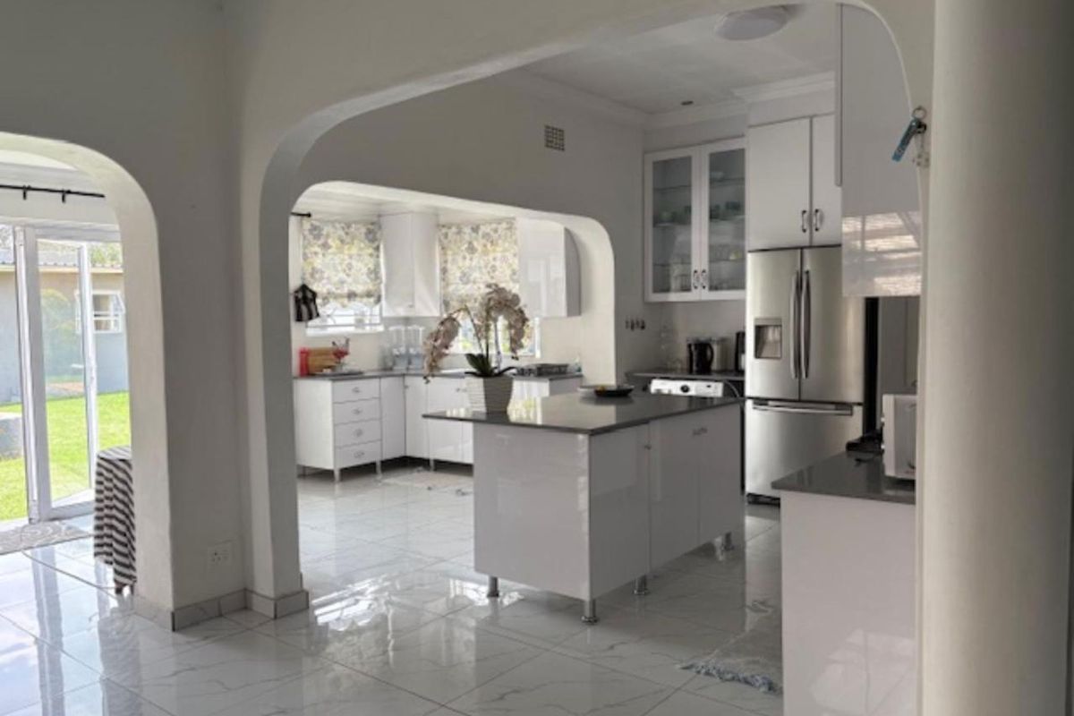 Modern kitchen featuring white cabinetry, a central island with stone countertops, and polished tiled flooring, seamlessly connected to the living area via an archway.
