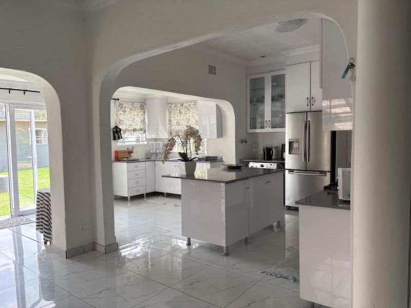 Modern kitchen featuring white cabinetry, a central island with stone countertops, and polished tiled flooring, seamlessly connected to the living area via an archway.