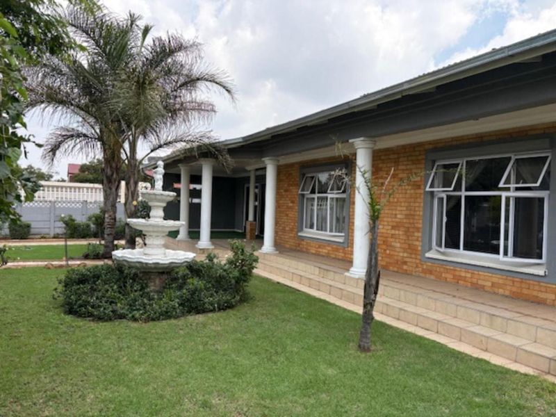 Front elevation of a brick house featuring a covered patio with columns, tiled steps, and a landscaped garden with a central fountain.