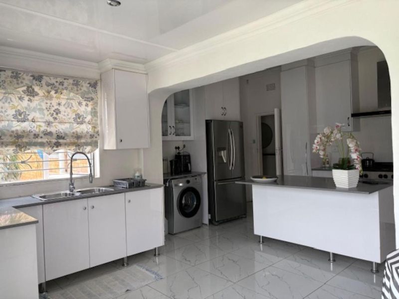A modern, well-lit kitchen featuring white cabinetry, stone countertops, a central island, and tiled flooring with a clean, functional layout.