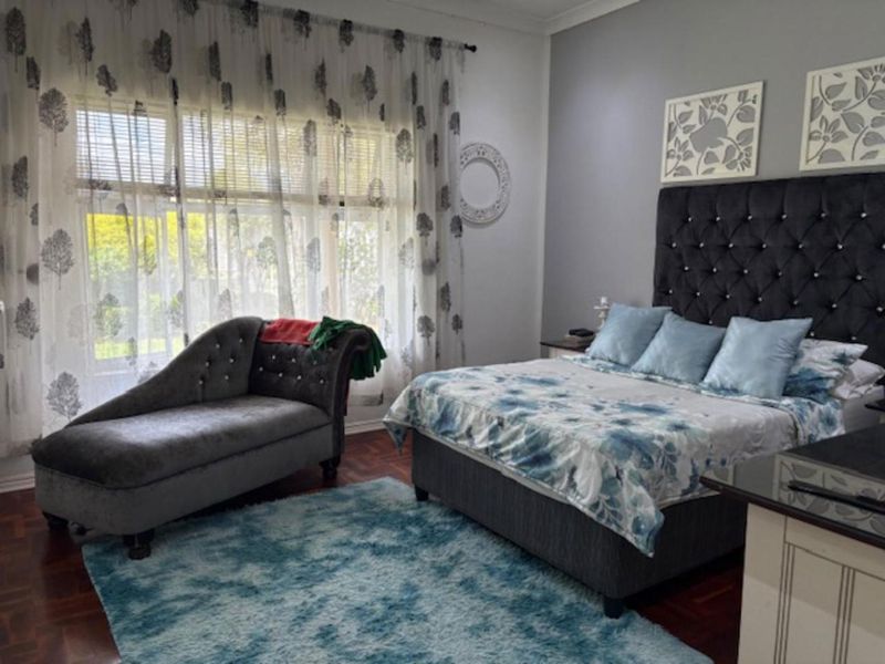 A spacious bedroom featuring warm parquet flooring, a large window allowing natural light, and classic cove cornicing.