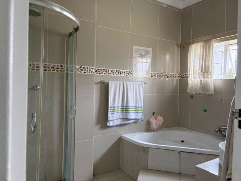 A functional bathroom featuring a corner bathtub, a separate glass-enclosed shower, and neutral wall tiling throughout.