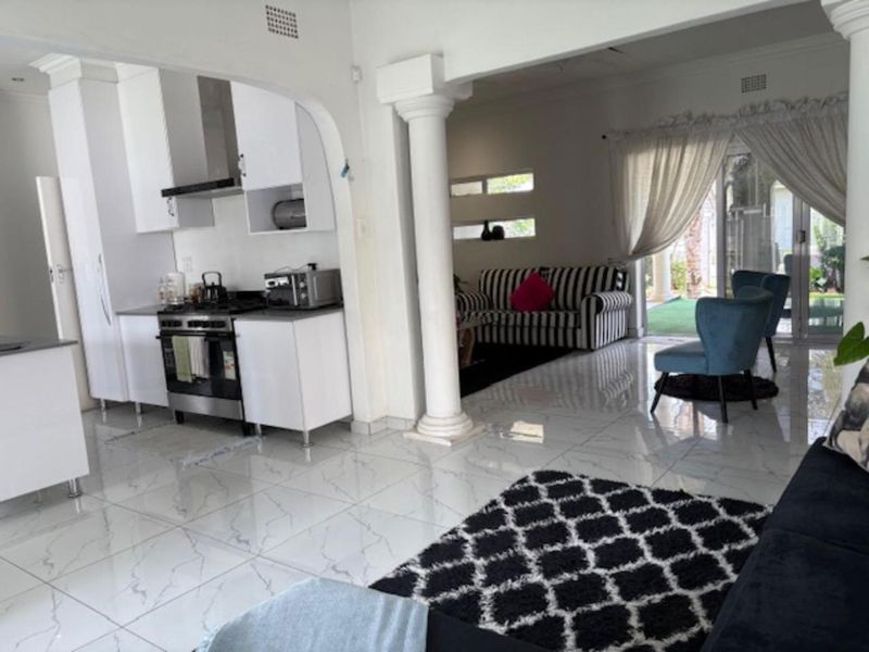 Open-plan living area featuring a modern kitchen with white cabinetry, gas stove, and sleek porcelain tiled flooring, seamlessly connecting to the lounge and patio.
