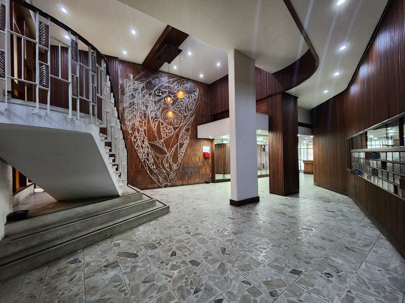 Spacious apartment building entrance lobby featuring classic terrazzo flooring, warm wood wall paneling, a feature staircase, and integrated mailboxes.