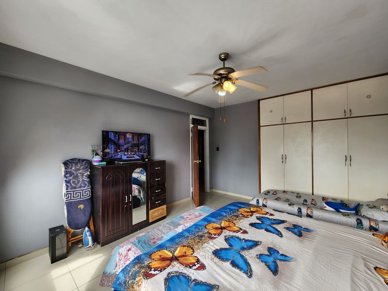 A bedroom featuring a ceiling fan, tiled flooring, and built-in wardrobe storage with grey painted walls.