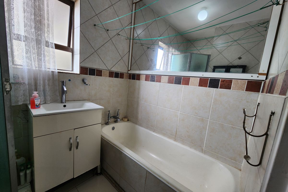 A functional bathroom featuring a built-in vanity with basin, a standard bathtub, and tiled walls with a large mirror.