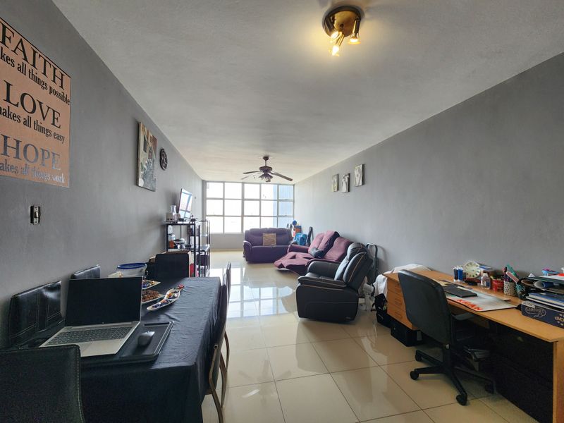 Spacious open-plan living and dining area featuring large windows, tiled flooring, and a ceiling fan, offering a versatile layout for modern apartment living.