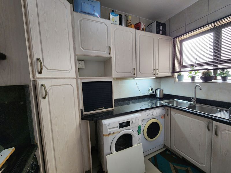 A compact kitchen featuring laminate cabinetry, granite countertops, a stainless steel sink, and integrated space for laundry appliances.