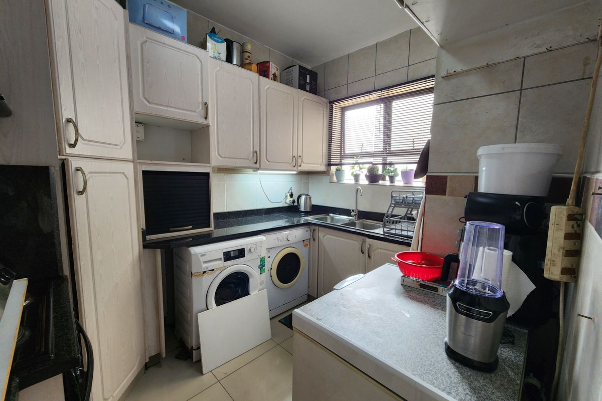 Compact kitchen featuring built-in cabinetry, granite countertops, and integrated laundry appliances, offering a functional layout with potential for modernization.