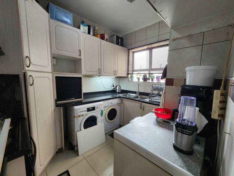 Compact kitchen featuring built-in cabinetry, granite countertops, and integrated laundry appliances, offering a functional layout with potential for modernization.