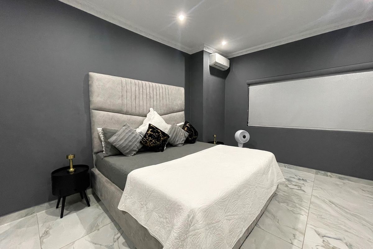 A modern bedroom featuring marble-look floor tiles, dark grey walls, recessed downlighting, and a wall-mounted split-system air conditioner.