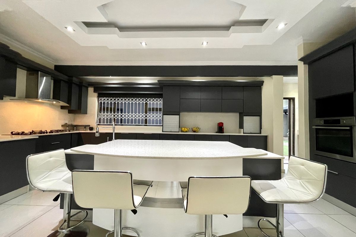 Modern kitchen featuring a central island, dark cabinetry, built-in oven, gas hob, and a decorative coffered ceiling with recessed lighting.
