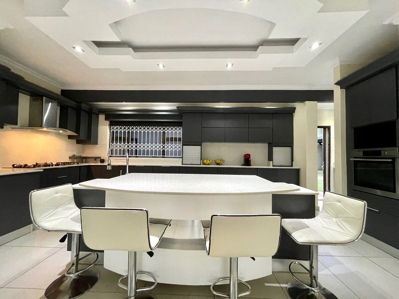 Modern kitchen featuring a central island, dark cabinetry, built-in oven, gas hob, and a decorative coffered ceiling with recessed lighting.