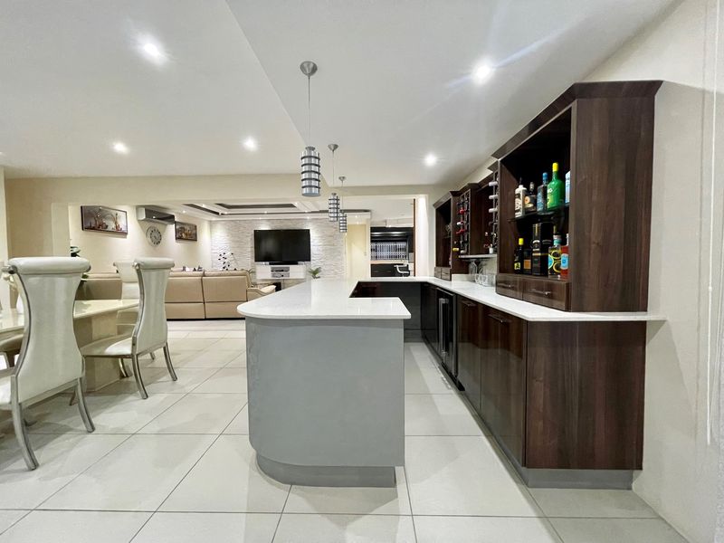 A modern, well-appointed home bar area featuring custom dark wood cabinetry, stone countertops, and integrated lighting, seamlessly connected to the open-plan living space.