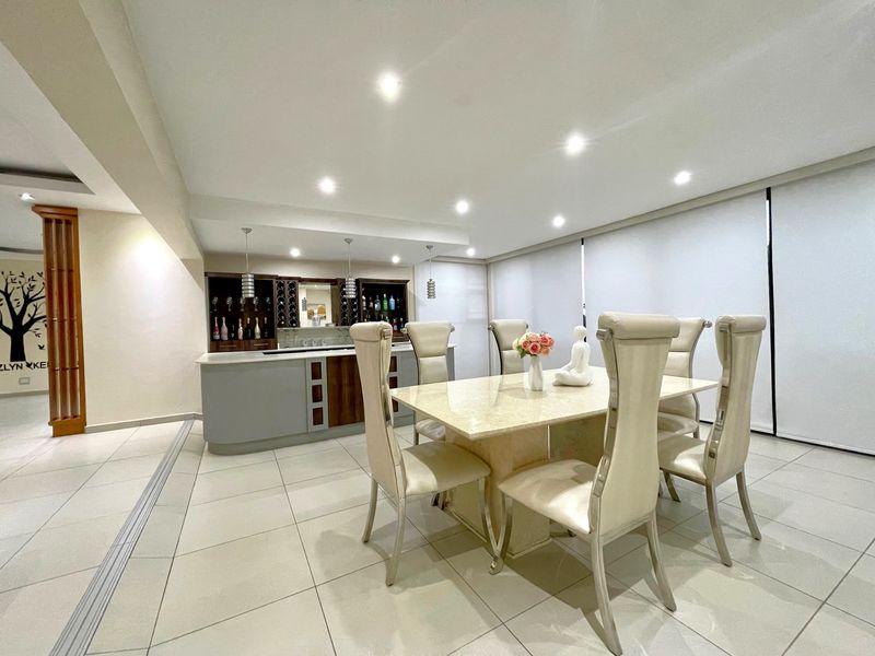 A well-maintained dining area featuring a built-in bar counter with integrated wine storage, recessed lighting, and neutral tiled flooring.