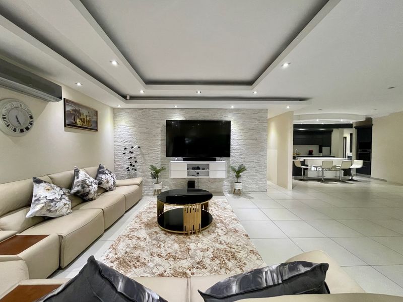 Spacious open-plan living area featuring a modern stone feature wall, recessed ceiling with downlights, and a seamless transition to a contemporary kitchen.