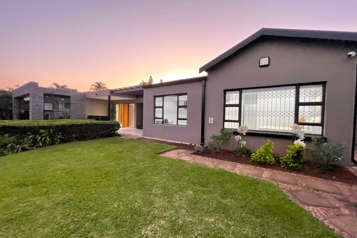 A well-maintained rear exterior view featuring a landscaped garden, paved walkway, covered patio area, and modern grey facade with security gates.